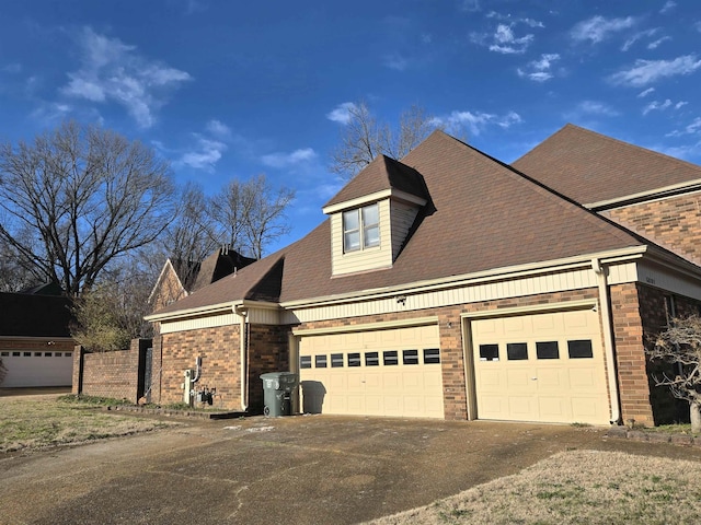 view of front of home with driveway, roof with shingles, a garage, brick siding, and fence