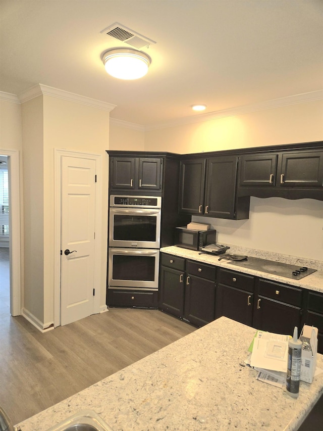 kitchen featuring stainless steel double oven, visible vents, dark cabinetry, and light wood-style floors