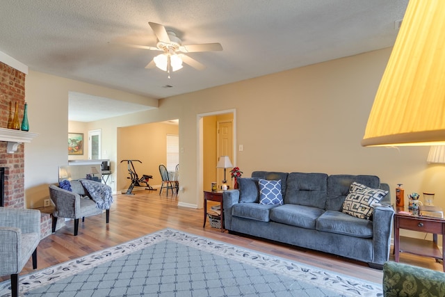 9995 Woodland Birch Dr, Lakeland, TN 38002 - living area featuring light wood-style flooring, a ceiling fan, a textured ceiling, baseboards, and a brick fireplace