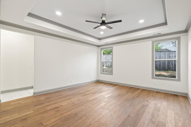 empty room featuring plenty of natural light, light wood-style floors, a raised ceiling, and ceiling fan