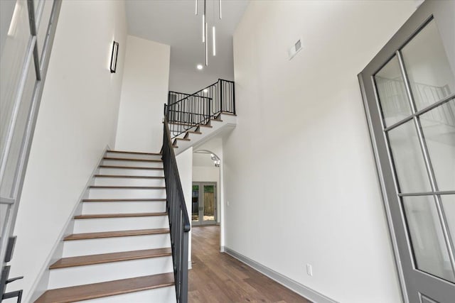 stairs featuring a high ceiling, wood finished floors, visible vents, and baseboards