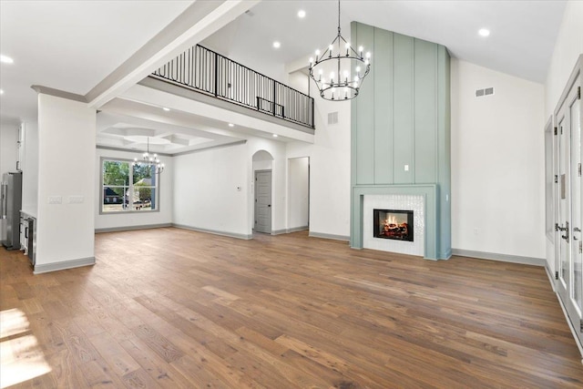 unfurnished living room featuring wood finished floors, arched walkways, an inviting chandelier, a large fireplace, and visible vents