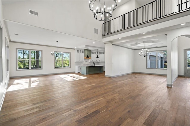 unfurnished living room featuring visible vents, a towering ceiling, baseboards, and an inviting chandelier