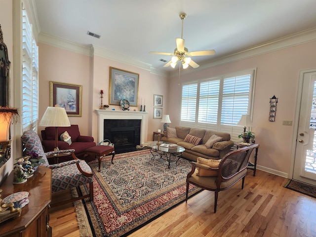 living room with light wood-type flooring, visible vents, ornamental molding, and ceiling fan