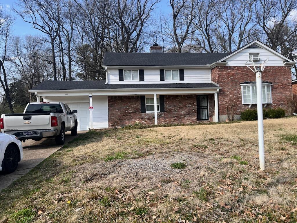 traditional home featuring driveway, a chimney, a front lawn, a garage, and brick siding