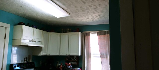 kitchen featuring under cabinet range hood, stove, white cabinets, and a textured ceiling