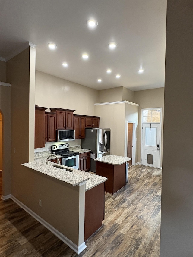 kitchen featuring light stone countertops, dark wood-type flooring, a peninsula, a kitchen island, and appliances with stainless steel finishes