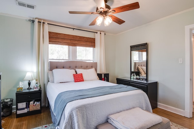 bedroom with multiple windows, wood finished floors, visible vents, and ornamental molding