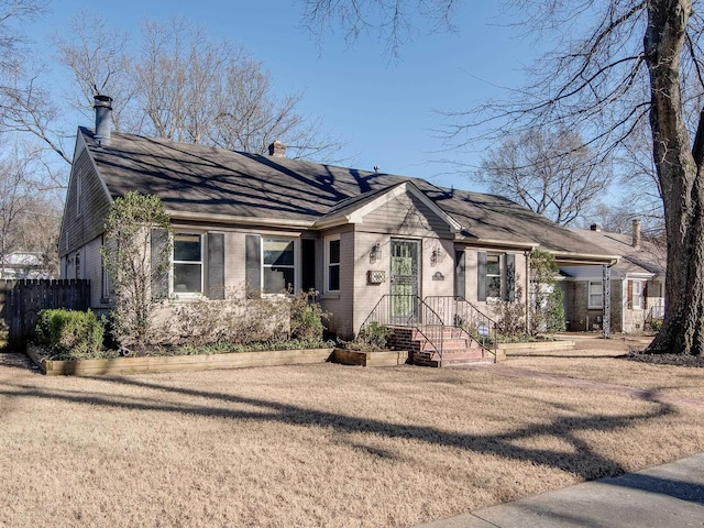 view of front of property with a front yard, brick siding, a chimney, and fence