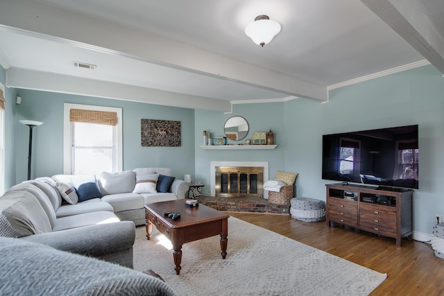 living area with visible vents, a brick fireplace, ornamental molding, beam ceiling, and wood finished floors