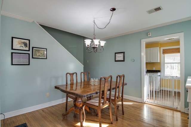 dining room with an inviting chandelier, light wood-style floors, visible vents, and ornamental molding