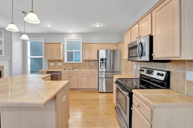 kitchen featuring tile counters, light brown cabinetry, light wood-style flooring, appliances with stainless steel finishes, and a sink