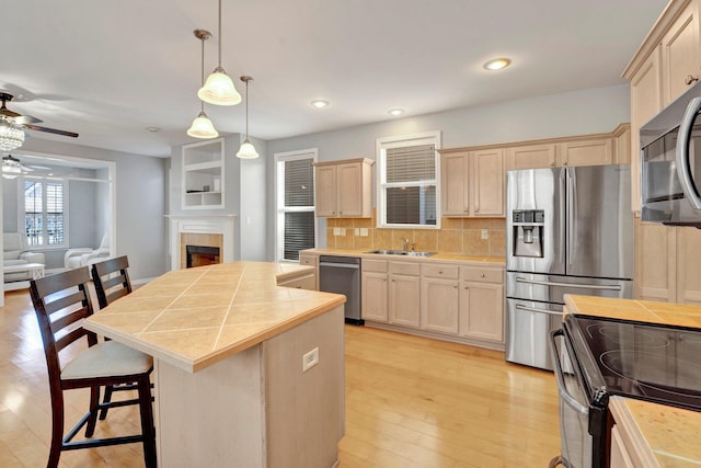 kitchen with a ceiling fan, light brown cabinets, backsplash, a center island, and stainless steel appliances