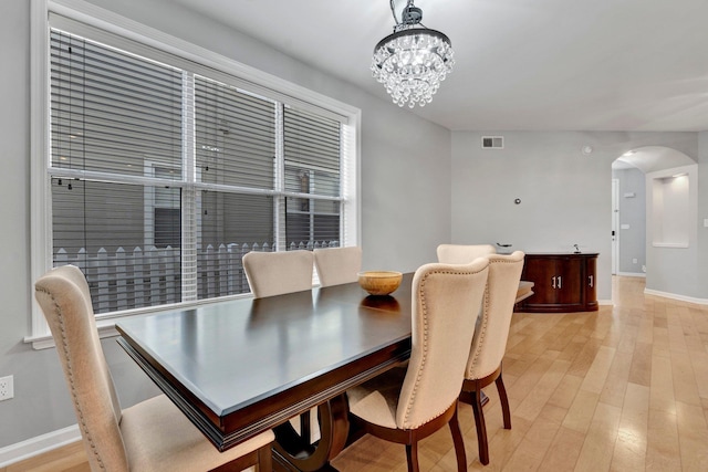 dining area featuring light wood-type flooring, visible vents, arched walkways, and a notable chandelier