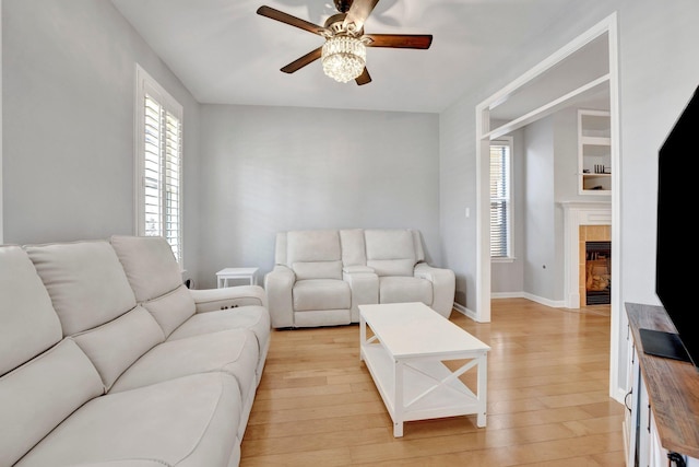 living area featuring a wealth of natural light, light wood-type flooring, ceiling fan, and a tiled fireplace