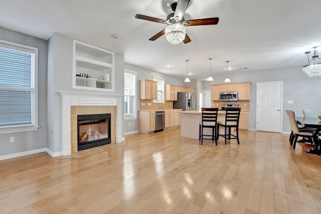 kitchen with light wood finished floors, light brown cabinetry, a kitchen bar, ceiling fan with notable chandelier, and appliances with stainless steel finishes