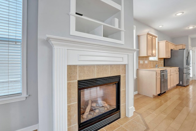 kitchen featuring light brown cabinets, backsplash, stainless steel appliances, a fireplace, and light countertops