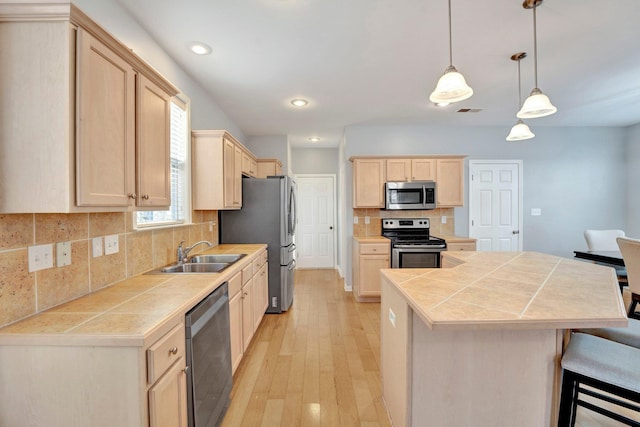 kitchen featuring light brown cabinets, a sink, appliances with stainless steel finishes, light wood-type flooring, and a center island