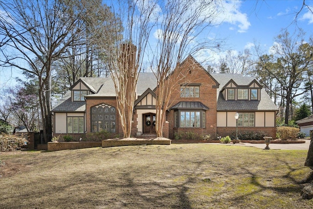 tudor home with stucco siding, brick siding, roof with shingles, and a front yard