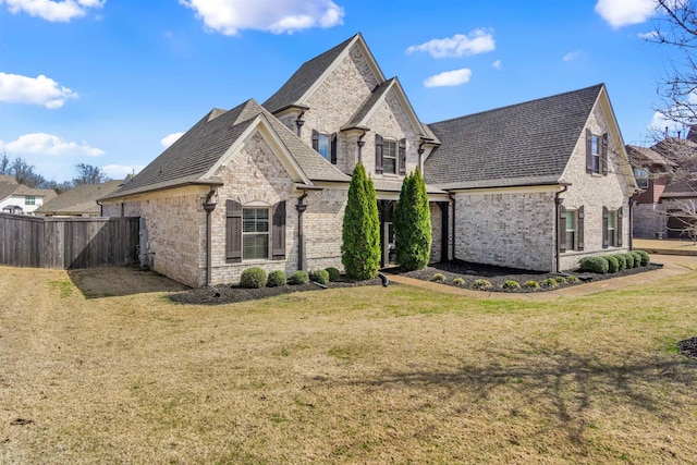 french provincial home with brick siding, a front yard, and fence