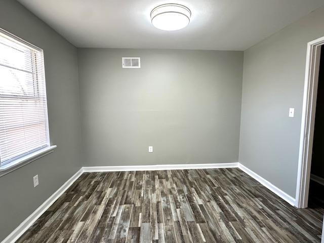 unfurnished room featuring baseboards, visible vents, and dark wood-style flooring