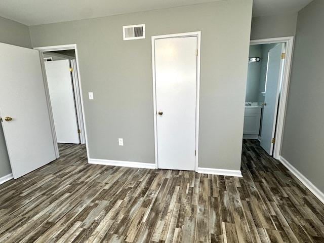 unfurnished bedroom featuring dark wood-style floors, visible vents, ensuite bathroom, and baseboards