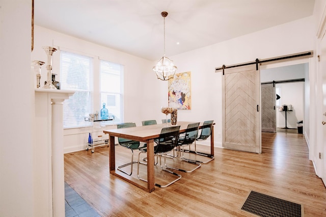 dining room featuring visible vents, a barn door, a notable chandelier, and light wood-style flooring