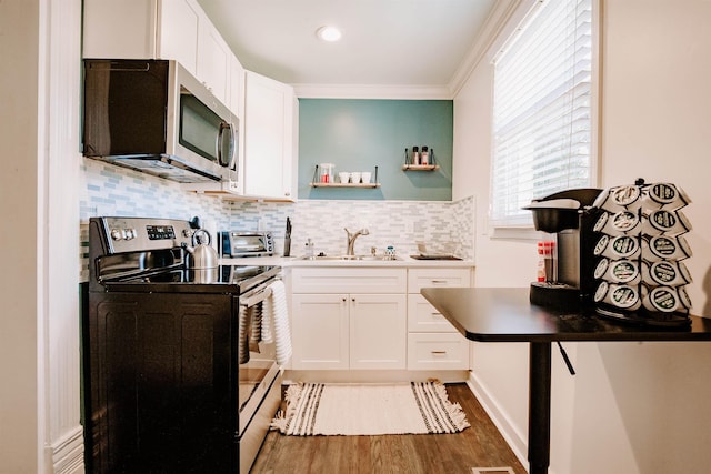 kitchen featuring a sink, tasteful backsplash, wood finished floors, white cabinetry, and stainless steel appliances