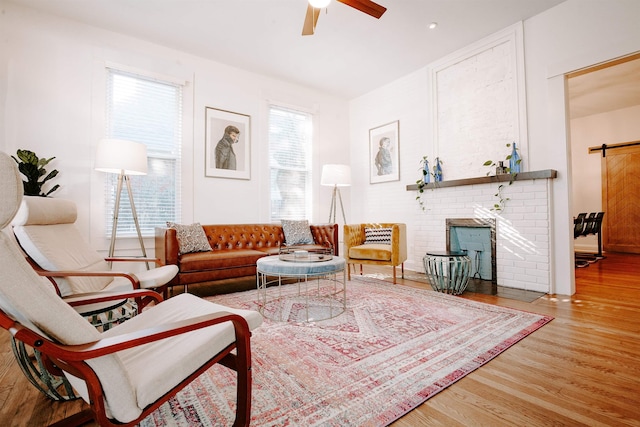 living room with a fireplace, wood finished floors, a barn door, and a ceiling fan