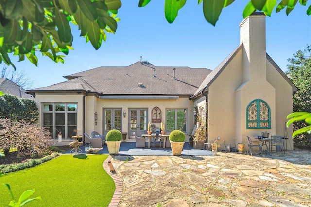 back of house featuring a chimney, roof with shingles, french doors, a patio, and brick siding