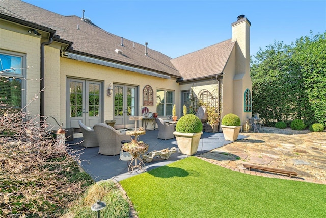 rear view of house featuring a chimney, roof with shingles, a patio area, french doors, and brick siding