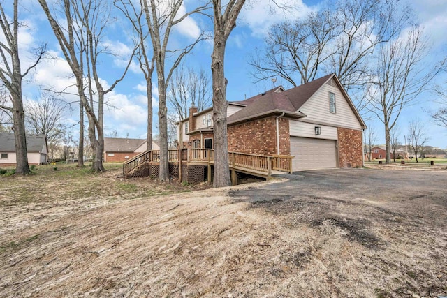 view of home's exterior featuring driveway, a chimney, a deck, brick siding, and a garage
