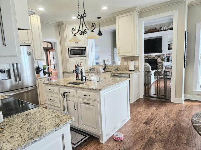 kitchen with a sink, a stone fireplace, stainless steel appliances, decorative light fixtures, and dark wood-style flooring