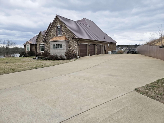 view of property exterior with driveway, stone siding, a standing seam roof, metal roof, and a lawn