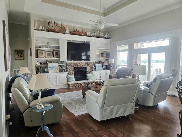 living room featuring a tray ceiling, dark wood-style floors, ornamental molding, and a stone fireplace