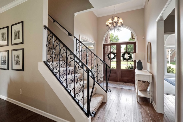 foyer with stairs, wood finished floors, a towering ceiling, ornamental molding, and an inviting chandelier