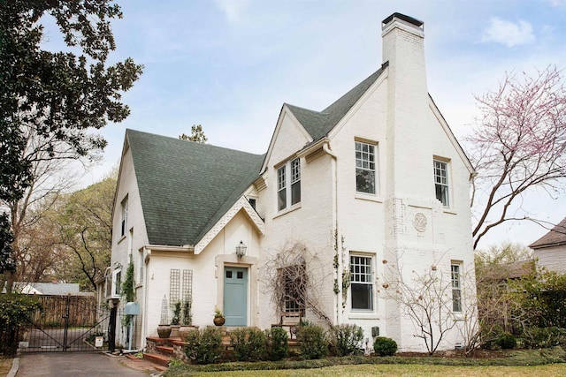 view of front of house with a gate, fence, a chimney, driveway, and a shingled roof