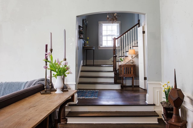 stairs featuring an inviting chandelier, arched walkways, and wood finished floors