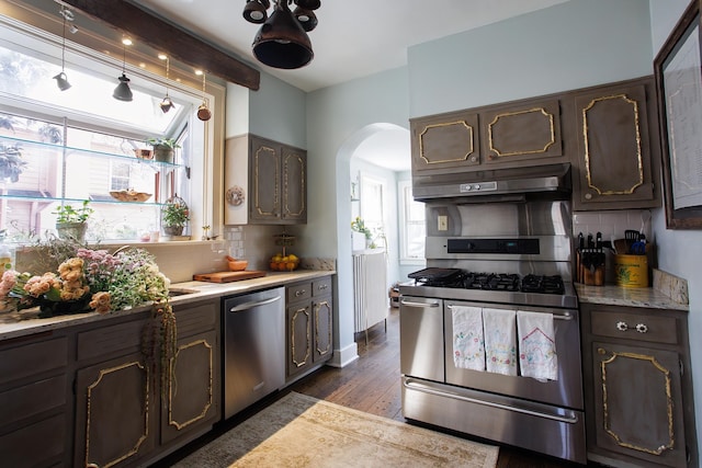 kitchen with light countertops, tasteful backsplash, arched walkways, under cabinet range hood, and appliances with stainless steel finishes