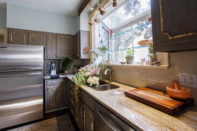 kitchen with a sink, backsplash, light stone countertops, appliances with stainless steel finishes, and dark brown cabinets