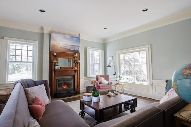 living room with a wainscoted wall, light wood-type flooring, crown molding, and plenty of natural light