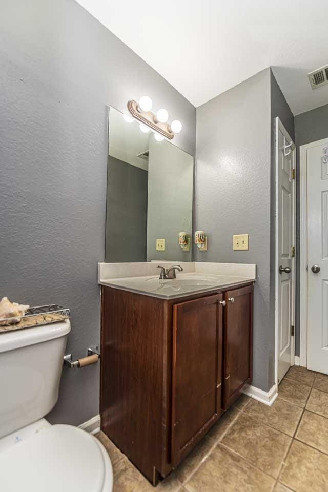 bathroom with tile patterned flooring, a textured wall, visible vents, toilet, and vanity
