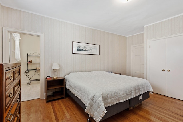 bedroom featuring a closet, wallpapered walls, light wood-style floors, and crown molding