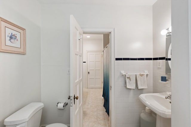 bathroom with tile walls, toilet, a sink, tile patterned flooring, and wainscoting