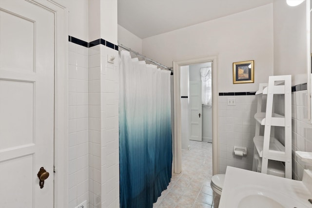 full bath with a shower with shower curtain, toilet, wainscoting, tile patterned flooring, and tile walls