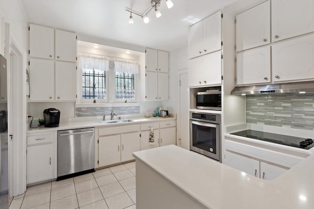 kitchen with under cabinet range hood, light tile patterned flooring, a sink, white cabinets, and appliances with stainless steel finishes