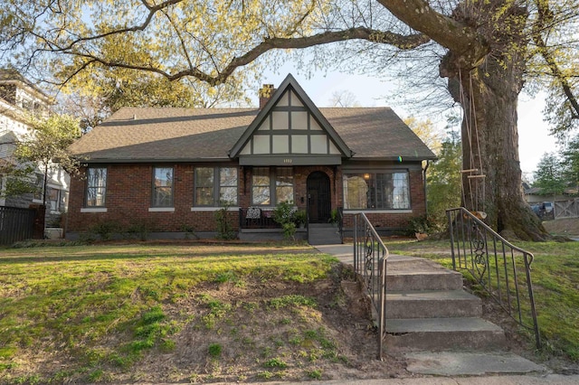 english style home with a chimney, a shingled roof, a front yard, and brick siding