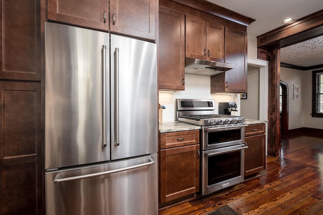 kitchen featuring dark wood-type flooring, under cabinet range hood, decorative backsplash, light stone counters, and appliances with stainless steel finishes
