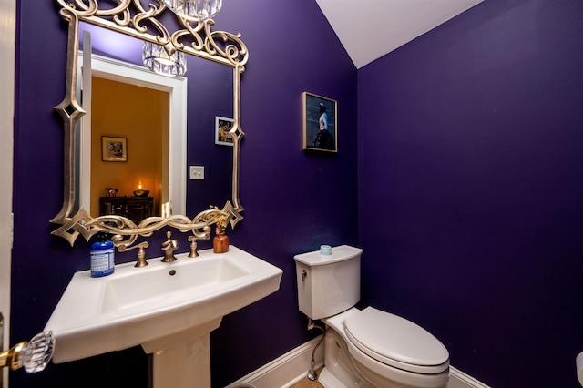 half bathroom with a notable chandelier, toilet, lofted ceiling, and a sink