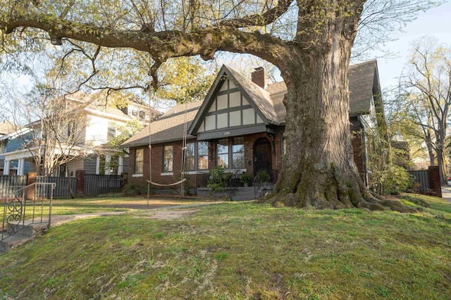view of front of home with fence, roof with shingles, a front yard, brick siding, and a chimney